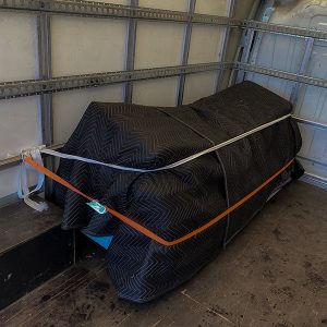 Sofa covered with black quilted removal blankets and secured in our van to show our man with a van service in Cornwall